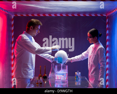 two scientists, a man and a woman, mixing chemicals in a containment tent, holding a glass container filled with a blue substanc Stock Photo