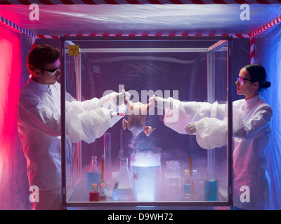 two scientists, a man and a woman, conducting chemical experiments on a raw chicken in a protection enclosure, in a containment tent Stock Photo