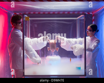 two scientists, a man and a woman, conducting chemical experiments on a raw chicken in a protection enclosure, in a containment tent Stock Photo