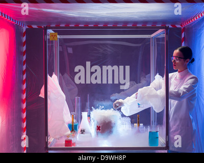 woman scientist conducting experiment with a steaming substance in a protection enclosure, in a containment tent Stock Photo