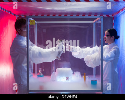 two scientists, a man and a woman, conducting experiments with a disco ball in a protection enclosure labeled as bio hazardous, Stock Photo