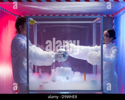 two scientists, a man and a woman, conducting experiments with a disco ball in a protection enclosure labeled as bio hazardous, Stock Photo