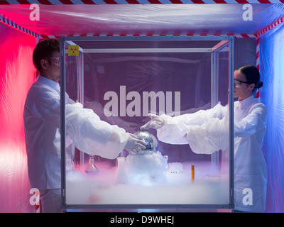 two scientists, a man and a woman, conducting experiments with a disco ball in a protection enclosure labeled as bio hazardous, Stock Photo