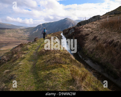 Walker follow leat around lower slopes of Y Braich in Snowdonia's Carneddau mountains. The leat feeds Llyn Cowlyd reservoir Stock Photo