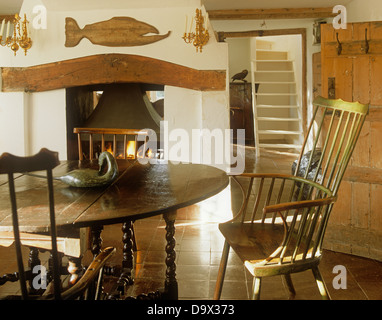 Antique oak table and stick back chairs in country dining room with rustic wooden fish and beam above fireplace Stock Photo