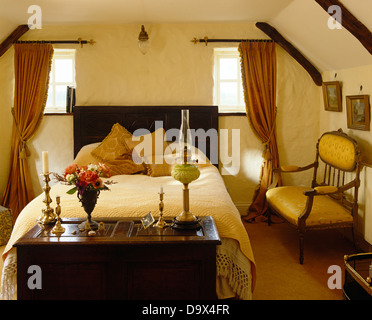 Old wooden chest at foot of double bed with cream bed cover in cottage bedroom with small Regency-style sofa Stock Photo