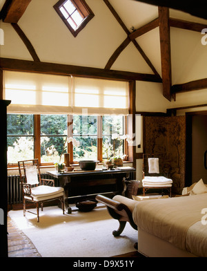 Tudor style beams and high vaulted ceiling in country bedroom with white blind on window above antique table Stock Photo
