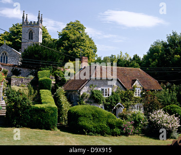 Clipped hedges in garden of old country vicarage set in front of church on small hilltop in English country village Stock Photo