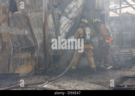 Two firefighters putting out a fire with a water hose Stock Photo