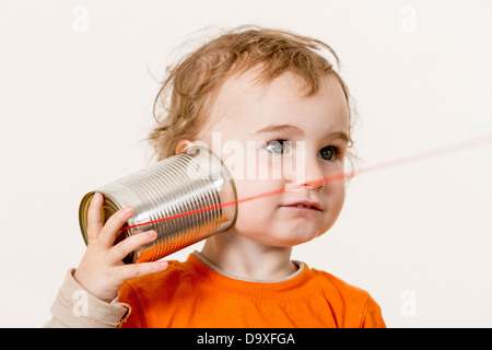 young child listening big to tin can phone. horizontal image with neutral light grey background Stock Photo