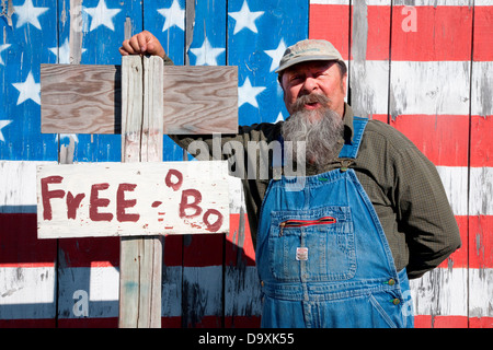 Howard the teacher poses in front of US flag and sign that says 'Free or Best Offer', near Augusta, Maine Stock Photo