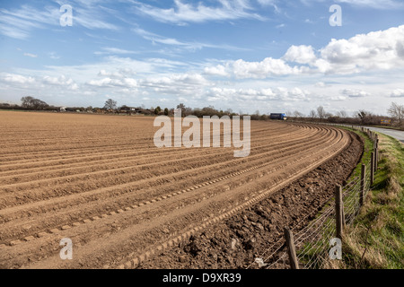 wide-angle view of ploughed field with vehicle on a bend of the road curving in and away from the RHS Stock Photo