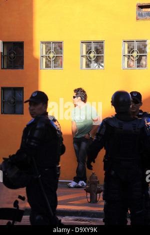 Man leans against wall while riot police stand on alert during Inti Raymi celebrations in Cotacachi, Ecuador Stock Photo