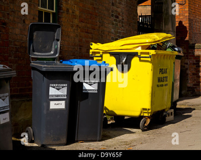 Black wheelie bins and yellow plastic skip used to collect domestic and commercial waste in a street in Wirksworth Derbyshire UK Stock Photo