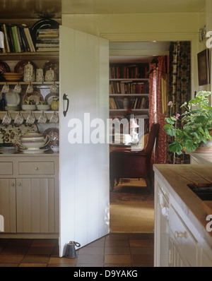 Cottage kitchen with china collection on lime washed dresser beside open door to cottage sitting room Stock Photo