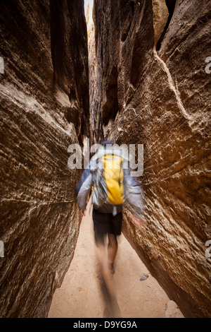 A man wearing a backpack walking through a narrow canyon while backpacking. Stock Photo