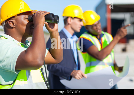 African construction worker using binoculars looking at construction site Stock Photo