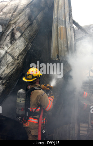 A firefighter spraying water on a structure fire hotspot Stock Photo