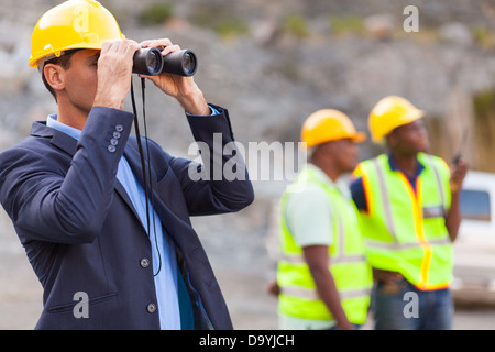 mine manager with binoculars at mining site Stock Photo