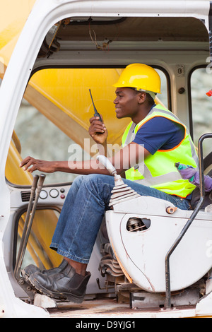 afro American man operates excavator while using walkie-talkie Stock Photo