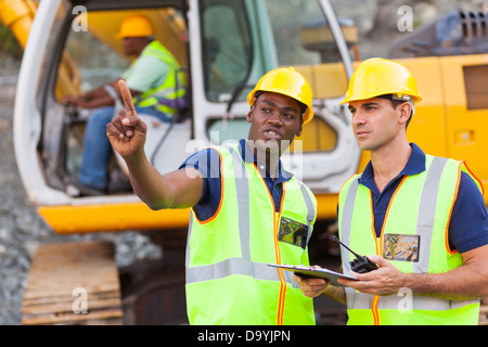 co-workers talking at construction site with bulldozer behind them Stock Photo