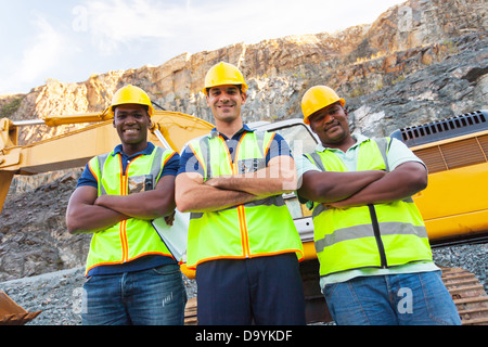 group of quarry workers standing next to excavator with arms crossed Stock Photo