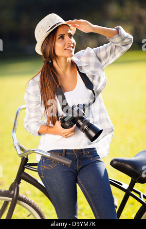 attractive casual young woman with camera and sitting on bicycle outdoors Stock Photo