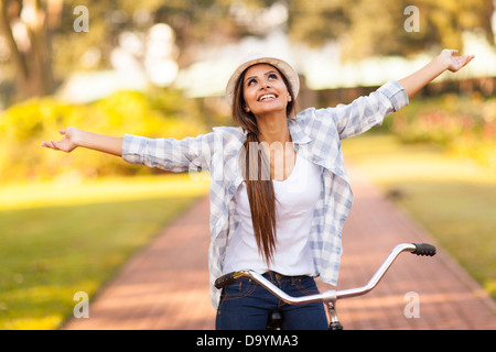 pretty young woman enjoying riding bike at the park with arms outstretched Stock Photo