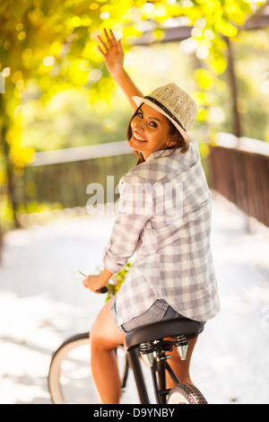 cheerful young woman riding her bike waving goodbye Stock Photo