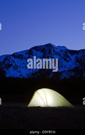 A tent is illuminated at dusk beneath Mount Tallac in Lake Tahoe, CA. Stock Photo