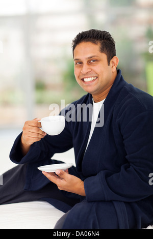 cheerful indian man in pajamas drinking coffee on bed Stock Photo