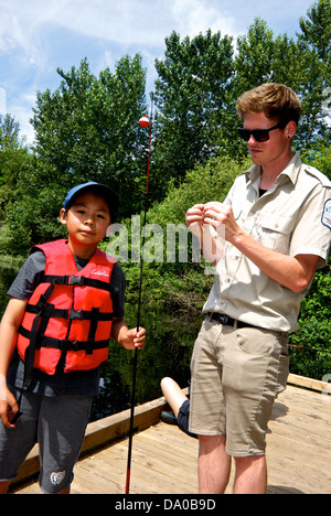 Freshwater Fisheries Society BC volunteer helping young Asian boy Learn to Fish program at Fishing in City Sanctuary Pond Stock Photo