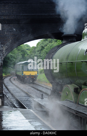 B12 class steam locomotive 8572 waits at Weybourne station as class 101 diesel multiple unit approaches on a rainy day, Norfolk Stock Photo