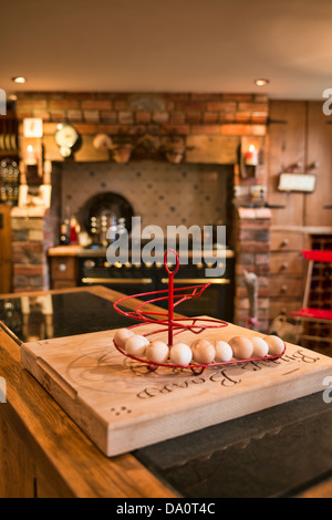 Fresh eggs on a stand on a bread board on a counter top island in a country kitchen Stock Photo