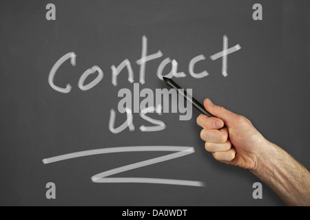 Mans hand pointing to a contact us message on a chalkboard. Stock Photo