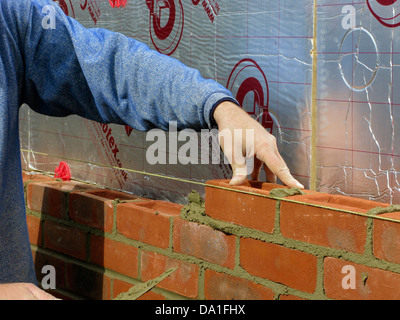 Builder cementing & building a brick wall with celotex thermal insulation board & cavity walls in an extension or new property Stock Photo