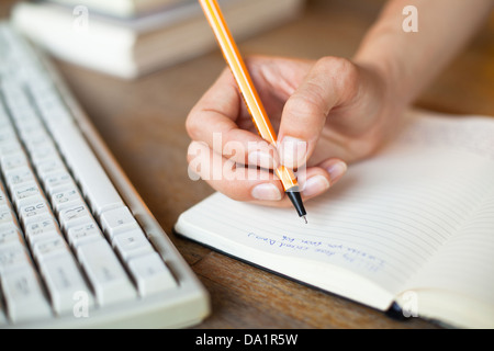 Hands writes a pen in a notebook, computer keyboard in background Stock Photo