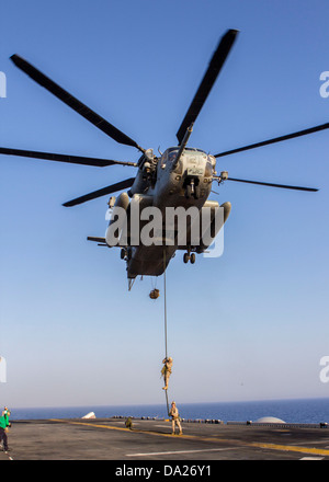 A US Marine assigned to Battalion Landing Team fast ropes from a CH-53 Super Stallion helicopter during familiarization training on the flight deck of the USS Kearsarge June 30, 2013. Stock Photo