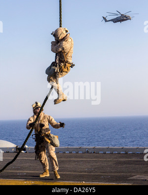 A US Marine assigned to Battalion Landing Team fast ropes from a CH-53 Super Stallion helicopter during familiarization training on the flight deck of the USS Kearsarge June 30, 2013. Stock Photo