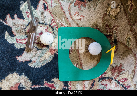 An indoor practice golf putting cup with two golf balls while a putter addresses the ball on a carpet. USA Stock Photo