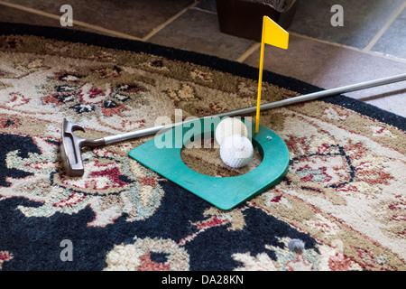 An indoor practice golf putting cup with two golf balls and a putter lying on a carpet. USA. Stock Photo