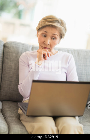 Senior woman sitting on sofa and using laptop Stock Photo