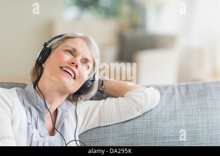 Senior woman sitting on sofa and listening to music Stock Photo