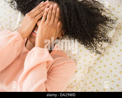 Woman lying down on bed, covering face with her hands Stock Photo