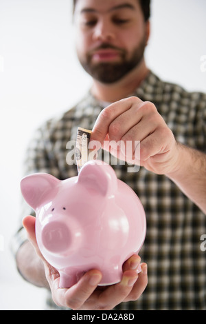Portrait of man holding piggy ban and putting money inside Stock Photo