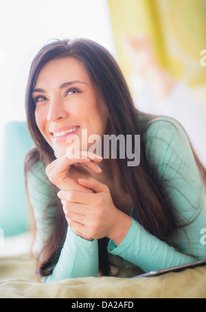 Portrait of woman lying down on bed with hand on chin, Looking up, Close-up Stock Photo