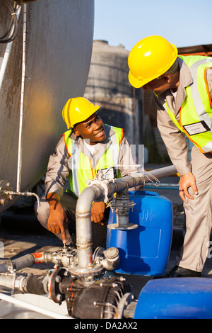 two petrochemical workers inspecting pressure valves on a fuel tank Stock Photo