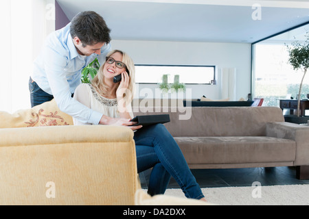 Woman talking on cell phone, man using tablet PC at home Stock Photo