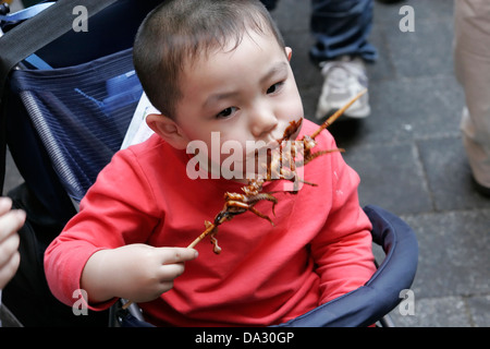 Chinese boy eating grilled octopus on the stick Wangfujing  street, Beijing, China Stock Photo