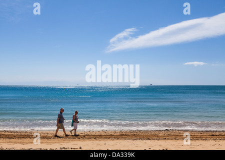 Middle aged couple walking along the waters edge on the beach. Stock Photo